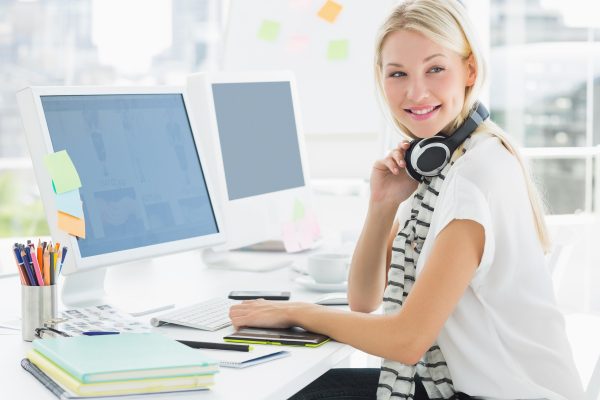Side view of a casual young woman with headset at computer desk in a bright office